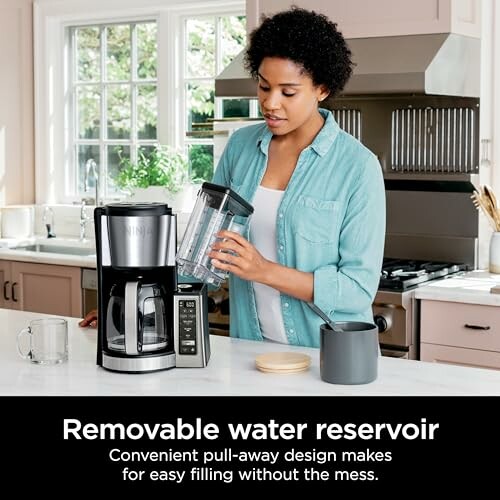 Woman using a coffee maker with removable water reservoir in a kitchen.